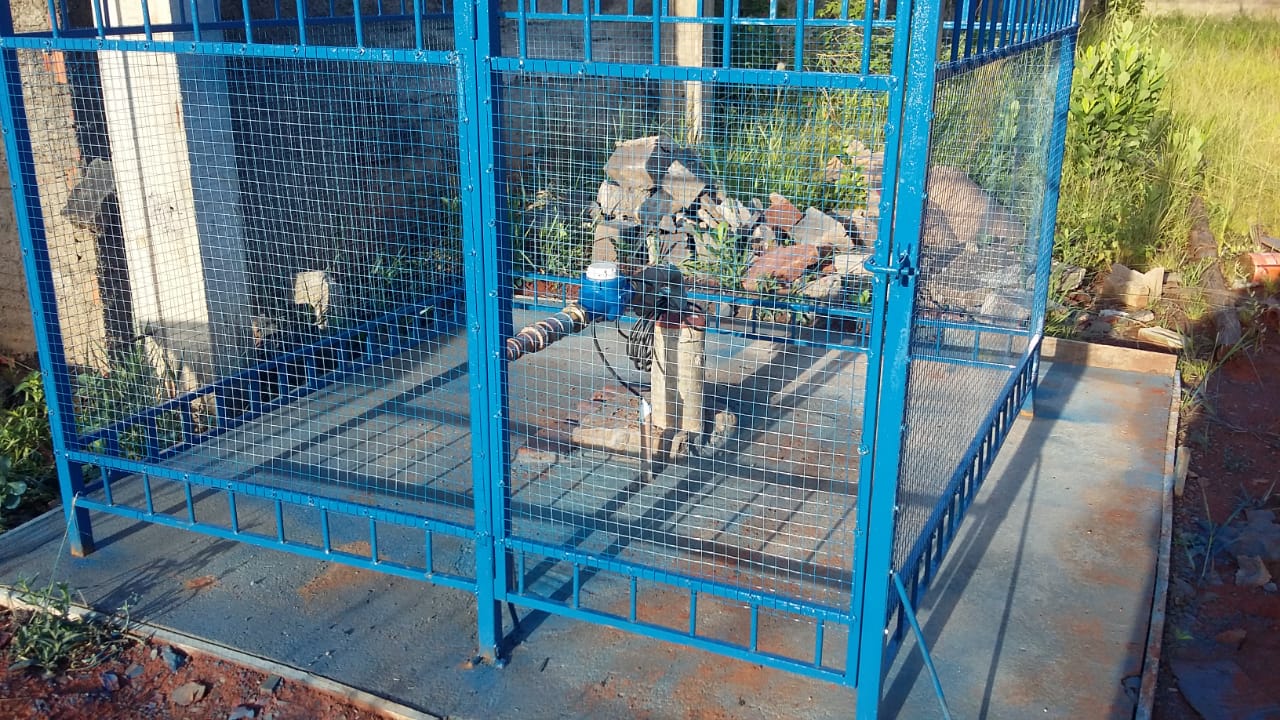 Cavalete de poço artesiano protegido por gaiola metálica azul de segurança, instalada sobre base de concreto.
